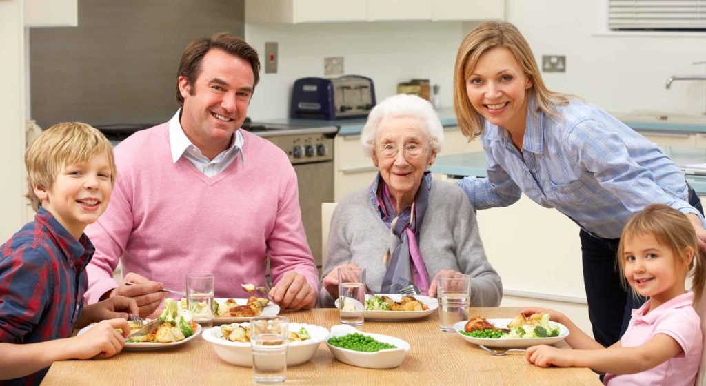 A younger family surrounding an elderly woman at the dinner table