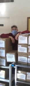 A Meals on Wheels volunteer standing above a stack of meal boxes