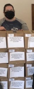A woman wearing a protective face mask stands behind stacks of boxed meals