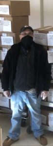A Meals on Wheels volunteer standing in front of stacks of meal boxes