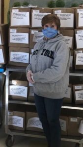 A woman wearing a protective face mask stands in front of a cart full of boxed meals