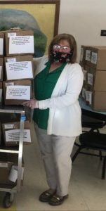 A woman wearing a protective face mask stands beside a cart full of boxed meals