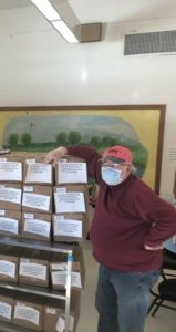 A man wearing a protective face mask stands beside stacks of boxed meals