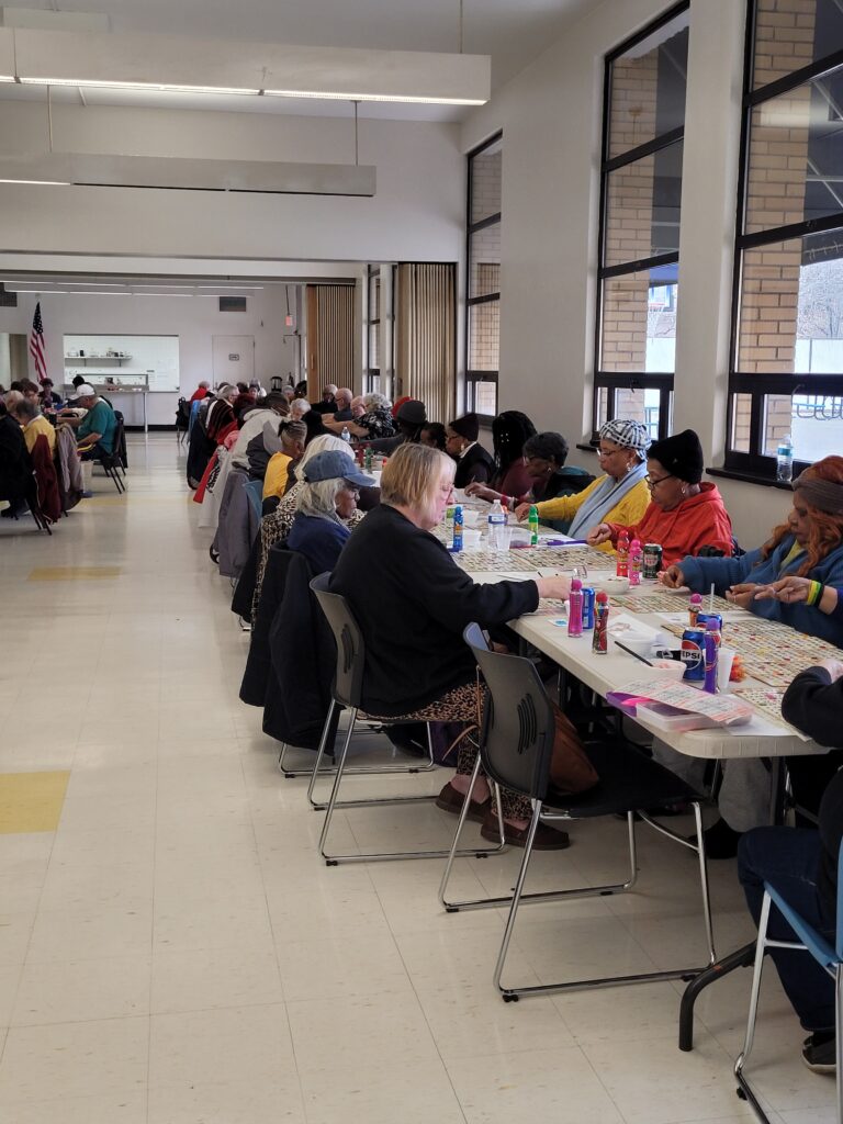 Group of older adults seated at long tables playing bingo together inside Turtle Creek Senior Center.