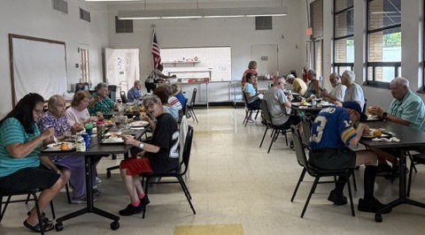 Older adult sitting at tables and having lunch in the great room at the senior center.